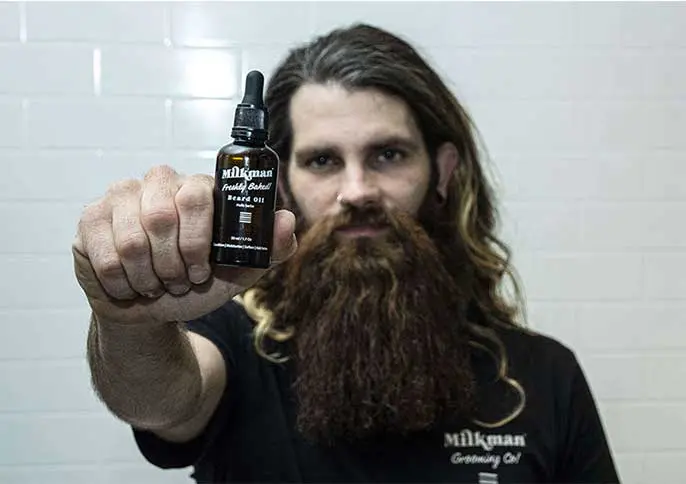 Man with a long beard holding up a bottle of Milkman beard oil, showing the product's typical male customer