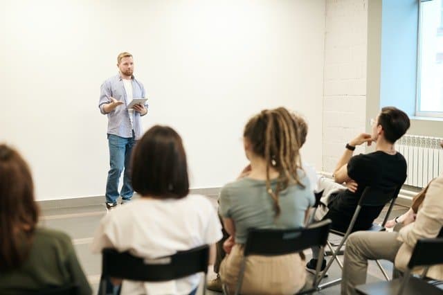 Presenter holding a tablet speaks to a seated audience, showing why knowing your audience matters