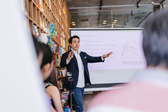Presenter speaking confidently to an attentive audience in front of a projected slide, showing the value of hooking people early