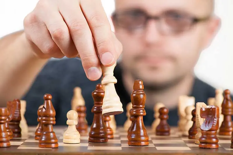 Man in glasses lifting a white chess piece over a board, illustrating strategic thinking behind networking for referrals