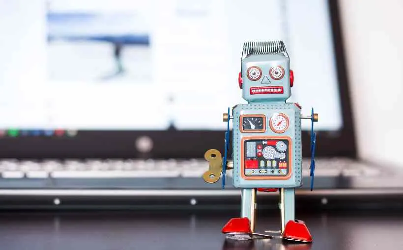 Retro wind-up toy robot standing in front of a laptop, representing the algorithms that shape what goes viral