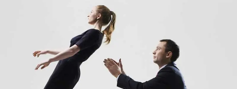 Woman in black falling backwards with arms out as a man in a suit kneels ready to catch her, illustrating trust