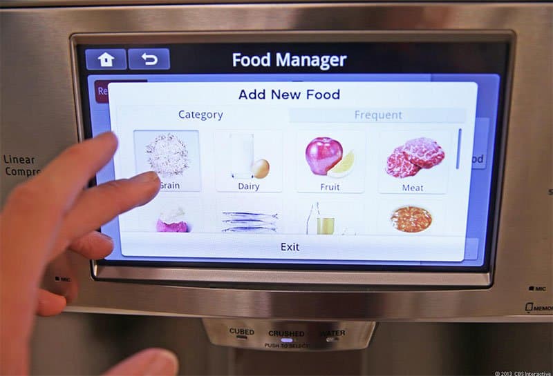 Hand touching a smart fridge's Food Manager screen, with an "Add New Food" menu showing grain, dairy, fruit and meat