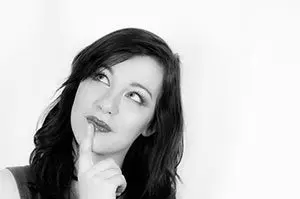 Black and white photo of a woman looking up thoughtfully with a finger to her lips, as if remembering a brand