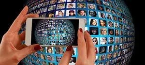 Hands holding a smartphone up to a globe made of hundreds of people's profile photos, showing a social audience