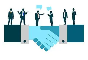 Illustration of a handshake with business people standing on the clasped hands, chatting, to show how familiarity builds trust